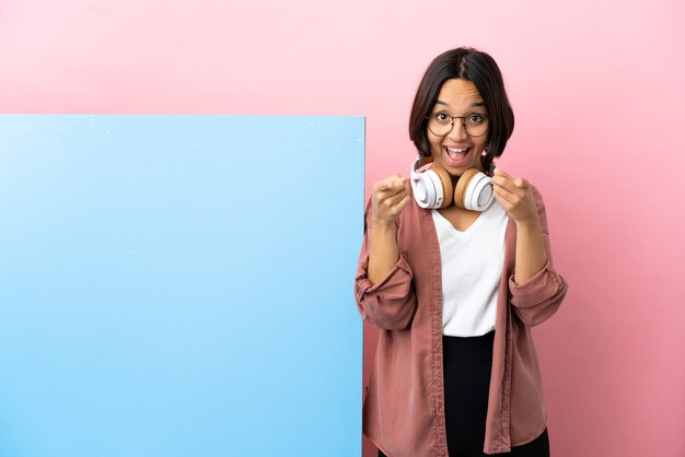 Jovem estudante mestiça com um grande banner sobre um fundo isolado surpresa e apontando para a frente