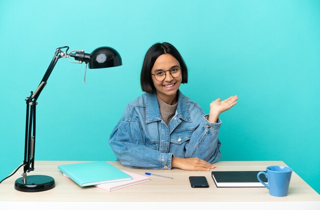 Jovem estudante mestiça estudando sobre uma mesa segurando o imaginário de copyspace na palma da mão para inserir um anúncio