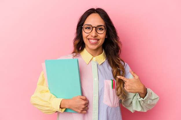 Jovem estudante mexicana isolada em fundo rosa pessoa apontando com a mão para um espaço de cópia de camisa, orgulhosa e confiante