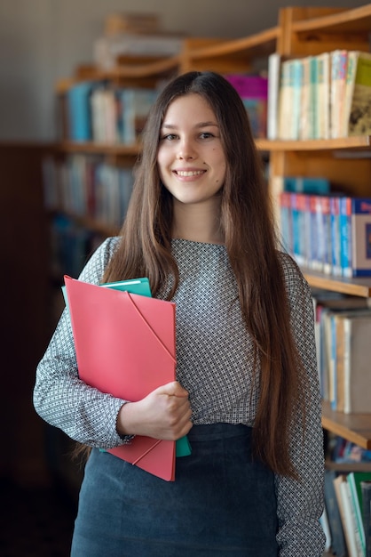 Jovem estudante na biblioteca ao lado de estantes prontas para aprender conhecimento educacional e conceito de pesquisa de literatura retrato de tiro vertical