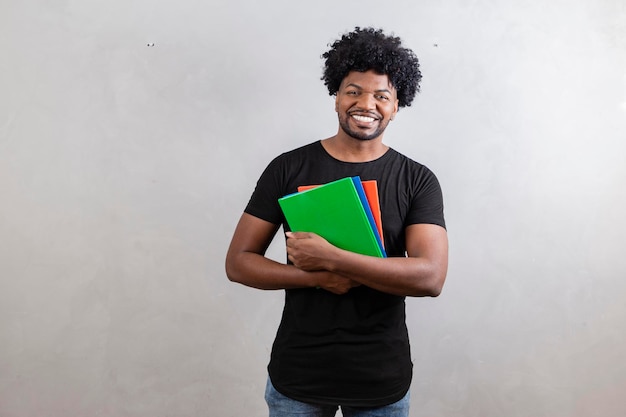 Jovem estudante negro com livros e cadernos no fundo