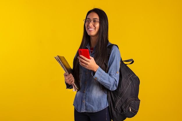 Jovem estudante segurando livros de mochila e olhando para celular em foto de estúdio