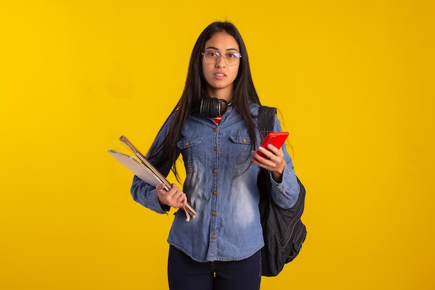 Jovem estudante segurando livros de mochila e olhando para celular em foto de estúdio