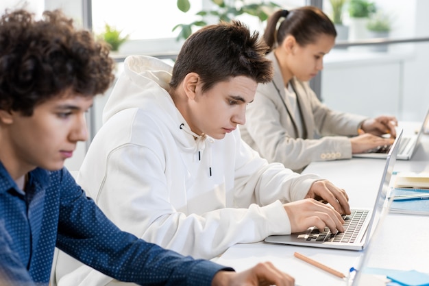 Jovem estudante sério olhando para dados na tela do laptop enquanto prepara a apresentação de um novo software entre colegas de classe