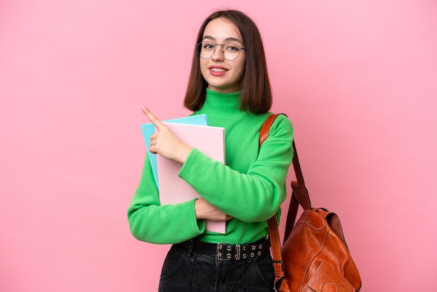 Jovem estudante ucraniana isolada em fundo rosa apontando para o lado para apresentar um produto