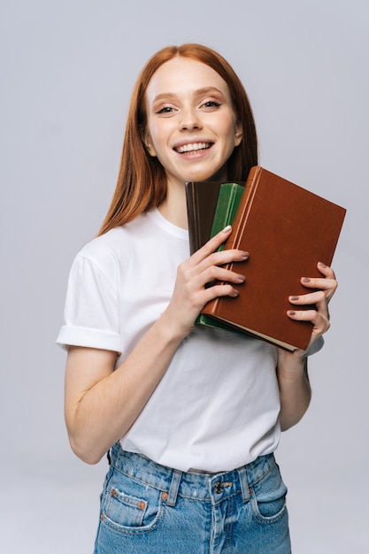 Jovem estudante universitária alegre segurando um livro e olhando para a câmera em um fundo isolado