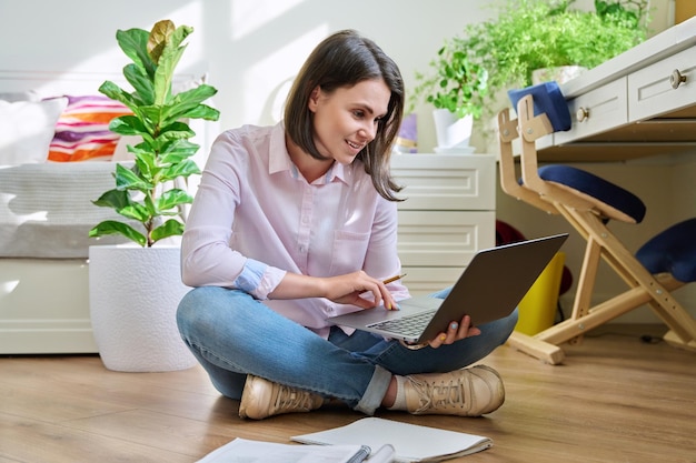 Jovem estudante universitária estudando em casa sentada no chão usando laptop E-learning e-educação auto-aprendizagem a distância aulas tecnologia conhecimento conceito de educação