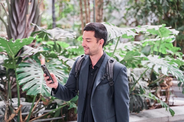 jovem estudante universitário em um blazer caminhando entre plantas com um telefone inteligente