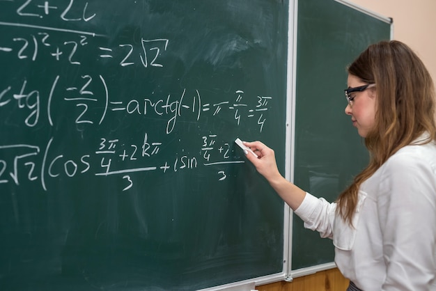 Jovem estudante universitário escrevendo exercícios matemáticos no quadro-negro durante uma aula. Educação