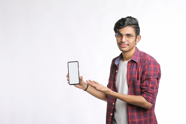 Jovem estudante universitário indiano mostrando a tela do smartphone em fundo branco.