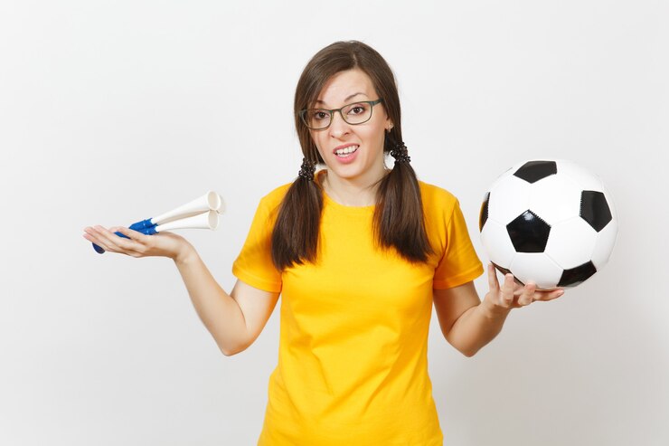 Foto jovem europeia triste chateada, dois divertidos rabos de cavalo, fã de futebol ou jogador de óculos, uniforme amarelo segurar o cachimbo de futebol, bola isolada no fundo branco. esporte, jogue futebol, conceito de estilo de vida.