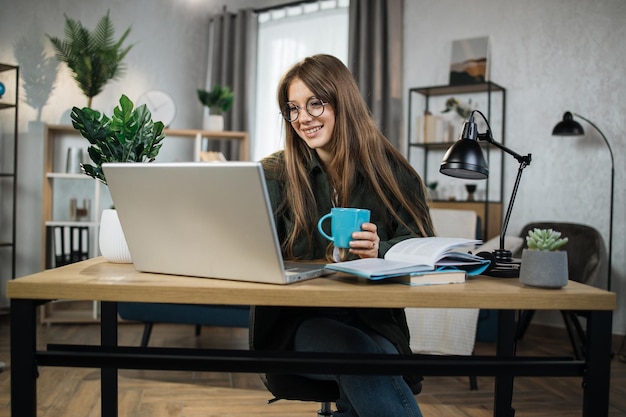 Jovem excitada sentada no local de trabalho com computador portátil e documento