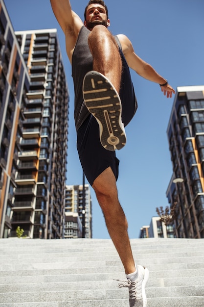 Jovem exercitando fora. Vista baixa do cara atlético desportivo saltando sobre a câmera. Mãos abertas. Exercício de atletista. Imagem vertical.