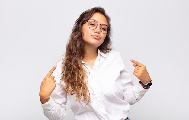 Foto jovem expressiva com óculos e blusa branca elegante posando na parede branca