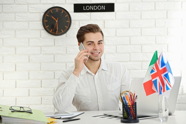 Jovem falando ao telefone inteligente no escritório de uma agência de viagens