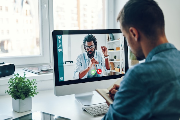 Jovem falando com o colega por videochamada enquanto está sentado no escritório