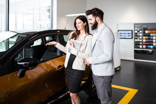 Jovem falando com vendedora e escolhendo um carro novo no showroom