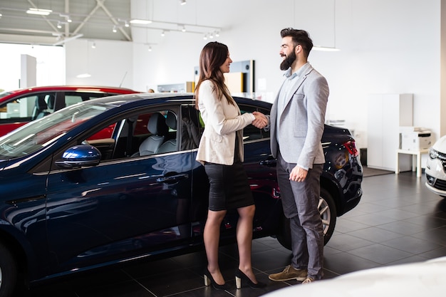 Jovem falando com vendedora e escolhendo um carro novo no showroom