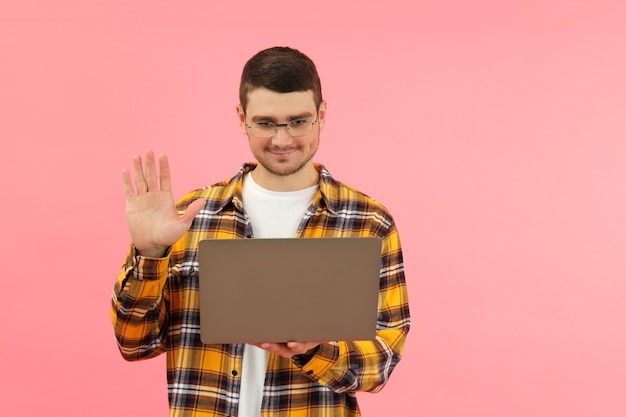 Jovem falando em comunicação por vídeo no laptop no fundo rosa.