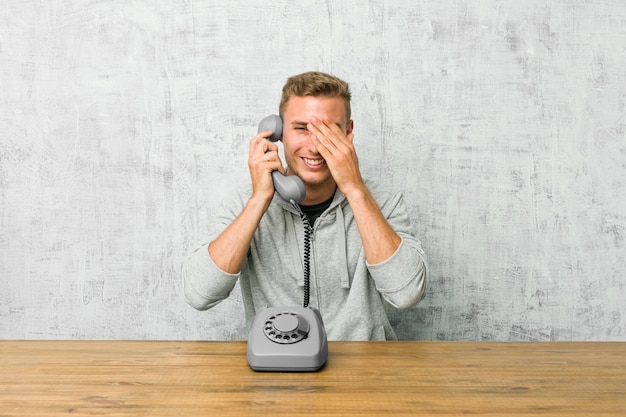 Jovem falando em um telefone vintage cobre os olhos com as mãos, sorri à espera de uma surpresa.