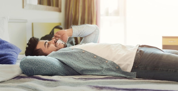 Jovem falando no celular enquanto relaxa na cama em um quarto de hotel