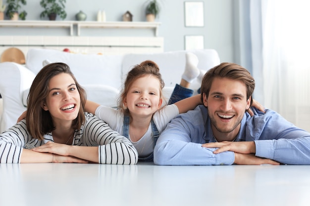 Jovem família caucasiana com filha pequena pose relaxar no chão da sala de estar, sorrindo, criança menina abraçar pais, mostrar amor e gratidão, descansar em casa juntos.