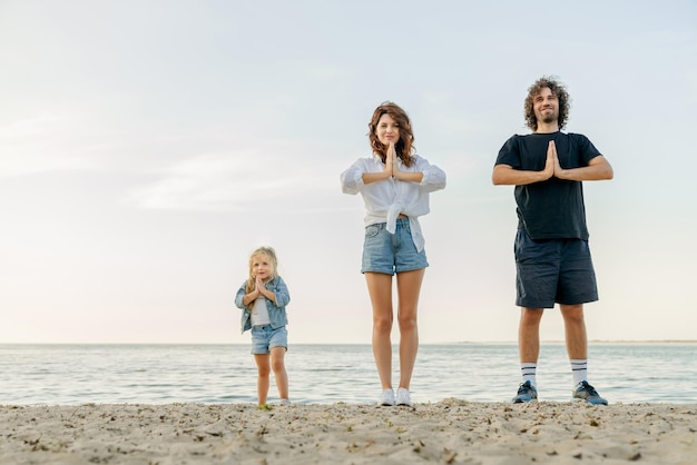 Jovem família caucasiana meditando juntos enquanto fazia ioga na praia