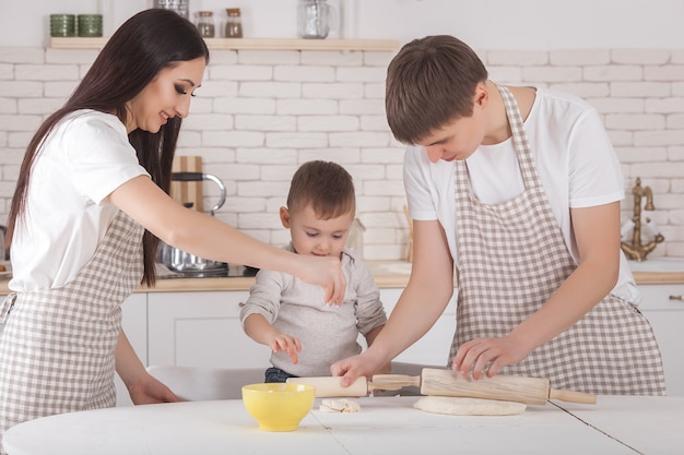 Jovem família cozinhando juntos. marido, esposa e seu bebê na cozinha. família amassar a massa com farinha. as pessoas cozinham o jantar ou café da manhã.