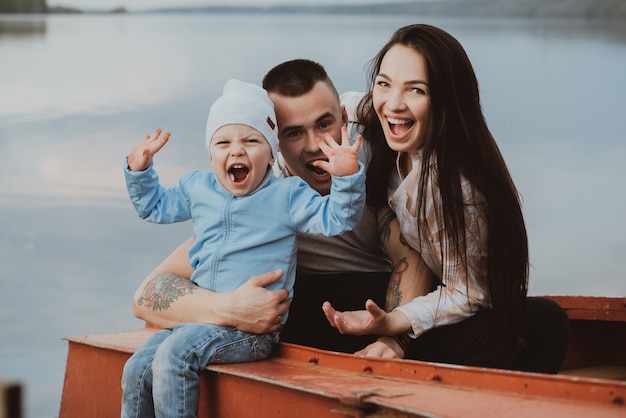 Jovem família feliz com seu filho sentado e sorrindo em um barco perto da água no verão