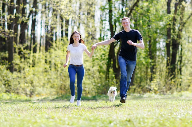 Jovem família feliz correndo com um cachorro em um prado verde