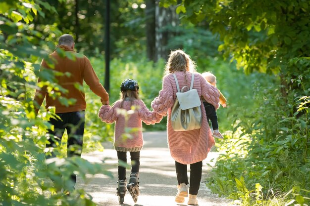 Jovem família feliz de pais e duas crianças andando na floresta mãe e pai segurando sua filha em rolos de skate pelas mãos