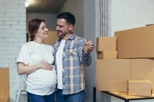 Jovem família feliz esperando um bebê Mulher grávida e marido se mudaram para um novo apartamento Desembale caixas com coisas Abraçando sorrindo