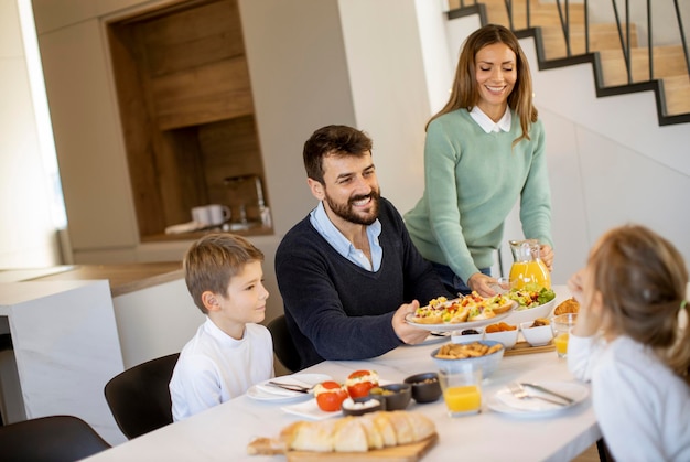 Jovem família feliz falando enquanto toma café da manhã na mesa de jantar no apartamento