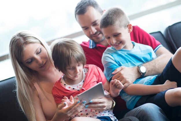 Foto jovem família feliz jogando juntos com o tablet em casa sentada no sofá