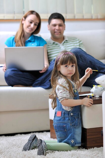 jovem família feliz na sala de estar brilhante e moderna, colocando dinheiro no cofrinho e trabalhando no computador portátil em finanças domésticas