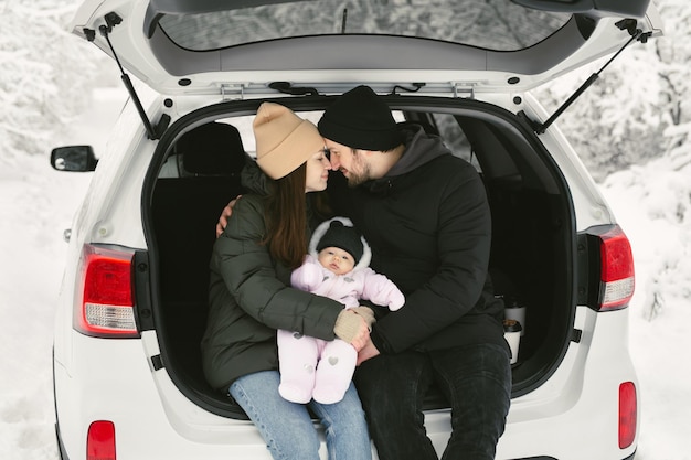 Jovem família feliz, um homem, uma mulher e um bebê estão sentados no porta-malas de um carro