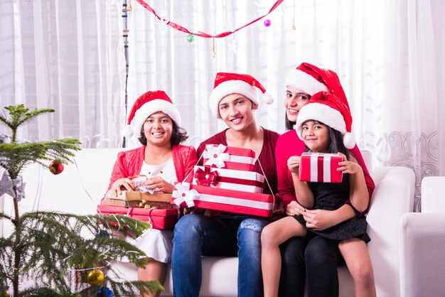 Jovem família indiana asiática comemorando o Natal com um presente usando chapéu de Papai Noel