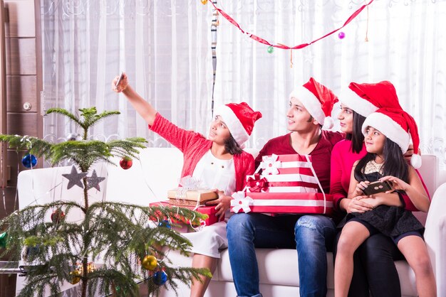 Jovem família indiana asiática comemorando o Natal com um presente usando chapéu de Papai Noel