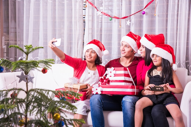 Jovem família indiana asiática comemorando o Natal com um presente usando chapéu de Papai Noel