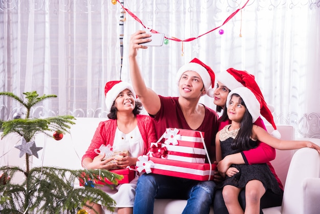 Jovem família indiana asiática comemorando o Natal com um presente usando chapéu de Papai Noel