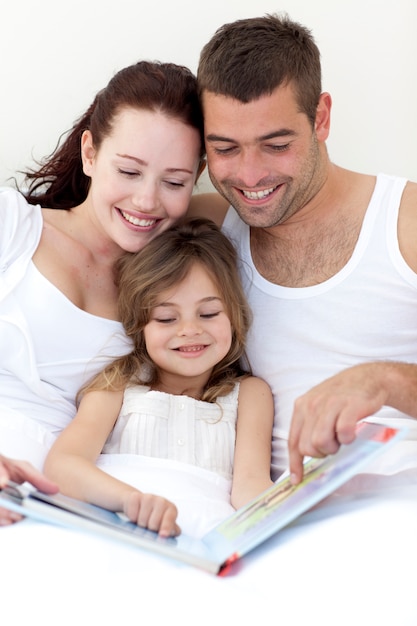 Foto jovem família lendo na cama