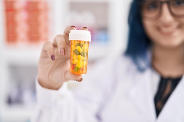 Jovem farmacêutica caucasiana sorrindo confiante segurando o frasco de comprimidos na farmácia
