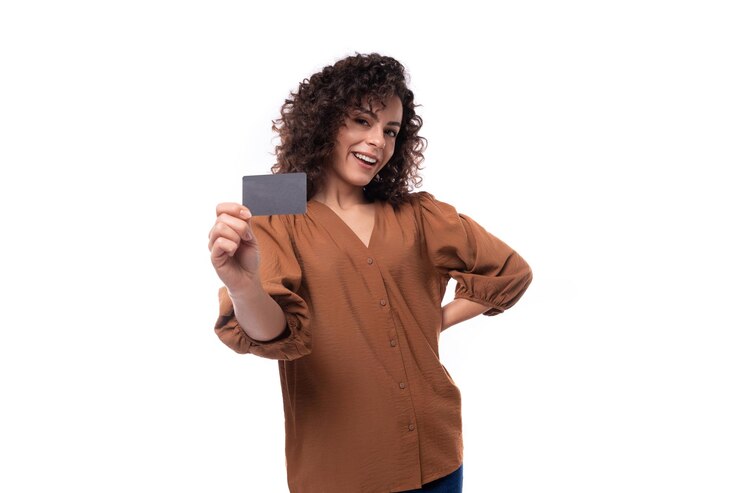 Jovem fashionista morena encaracolada vestida com uma elegante blusa marrom mostra um cartão de plástico