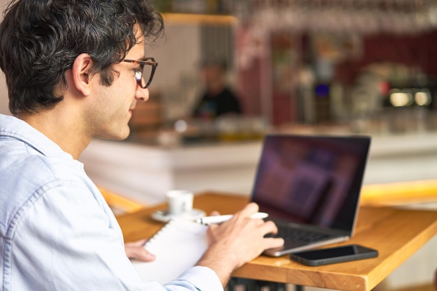 Jovem faz anotações enquanto trabalha no laptop no café aconchegante