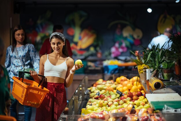 Foto jovem faz compras no supermercado escolhendo maçãs na loja