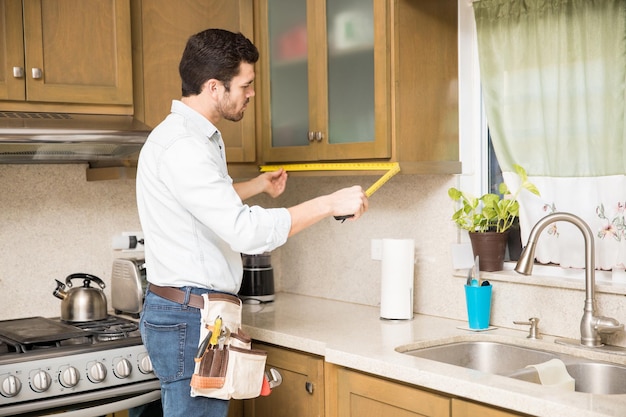 Jovem faz-tudo usando uma fita métrica para obter as dimensões de um armário de cozinha e fazer alguns reparos