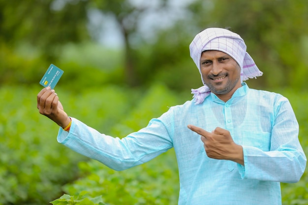 Jovem fazendeiro indiano mostrando cartão de débito ou crédito em seu campo de agricultura verde