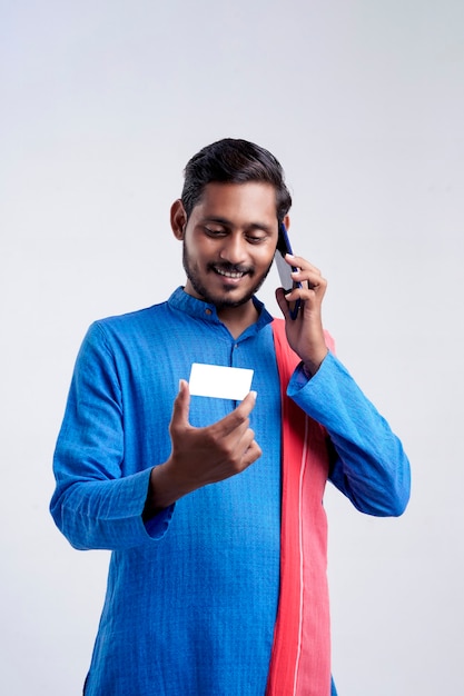 Jovem fazendeiro indiano mostrando cartão e falando no celular sobre fundo branco