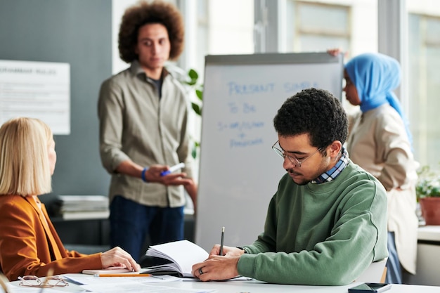 Jovem fazendo anotações no caderno enquanto está sentado à mesa na aula