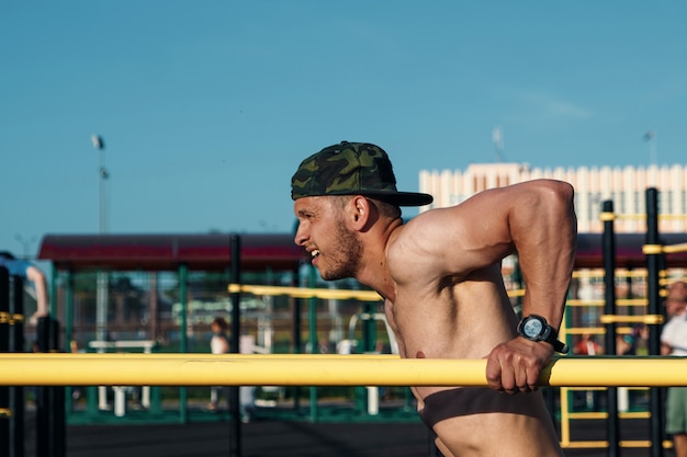 Jovem fazendo exercícios as barras irregulares no estádio, atleta, treinamento ao ar livre na cidade